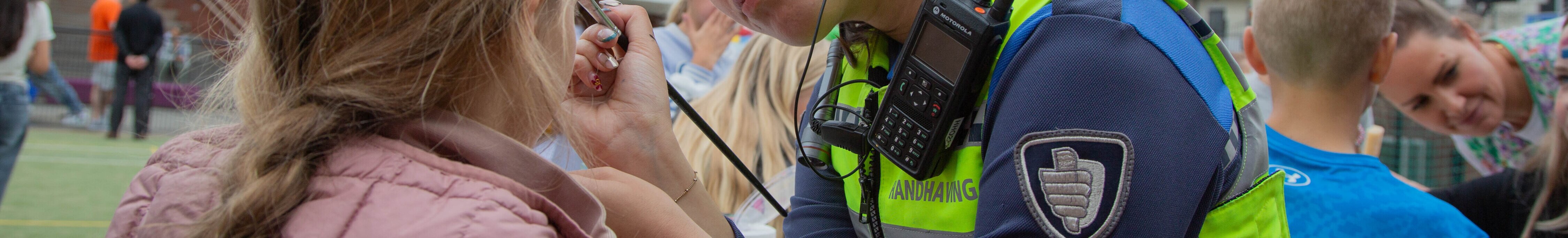 Handhaver schminkt een jong meisje tijdens een buurtactiviteit op een schoolplein.